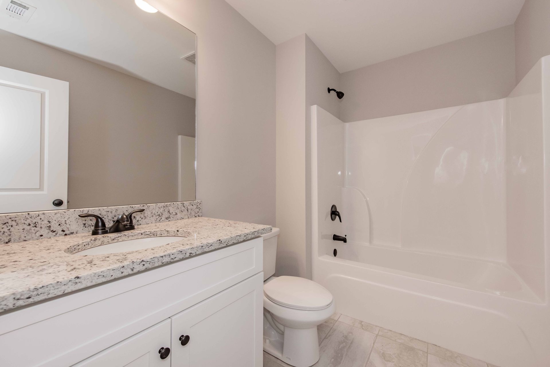 Modern bathroom with granite vanity, white toilet, and tub-shower combo
