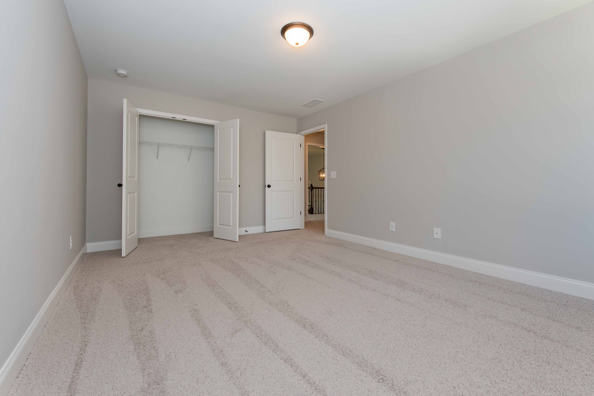 Empty beige carpeted bedroom with gray walls, closet doors, and a ceiling light.