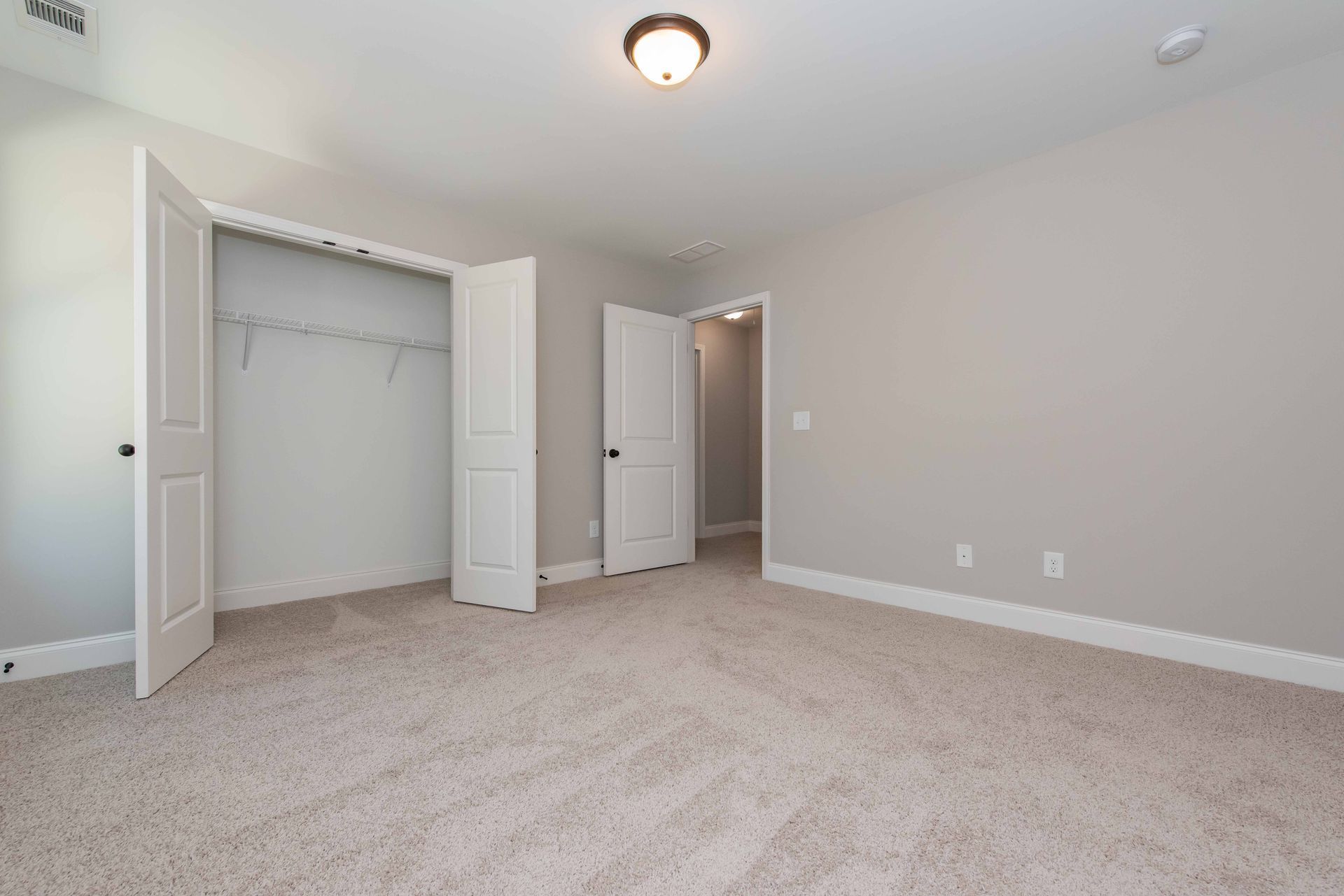 Empty beige bedroom with open closet doors, carpeted floor, and hallway door.
