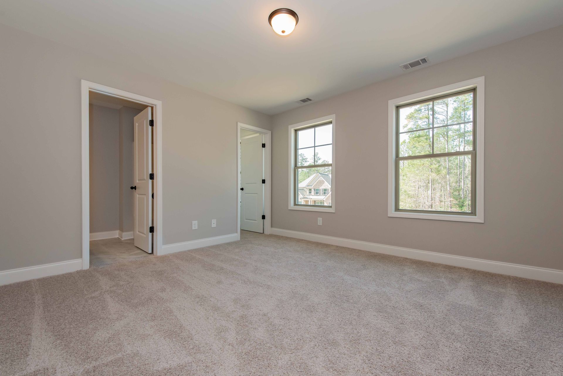 Empty beige bedroom with carpet, two windows, and open closet doors