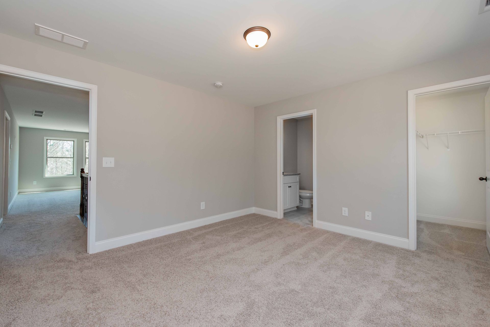 Empty beige bedroom with carpet, ceiling light, bathroom doorway, and closet entrance