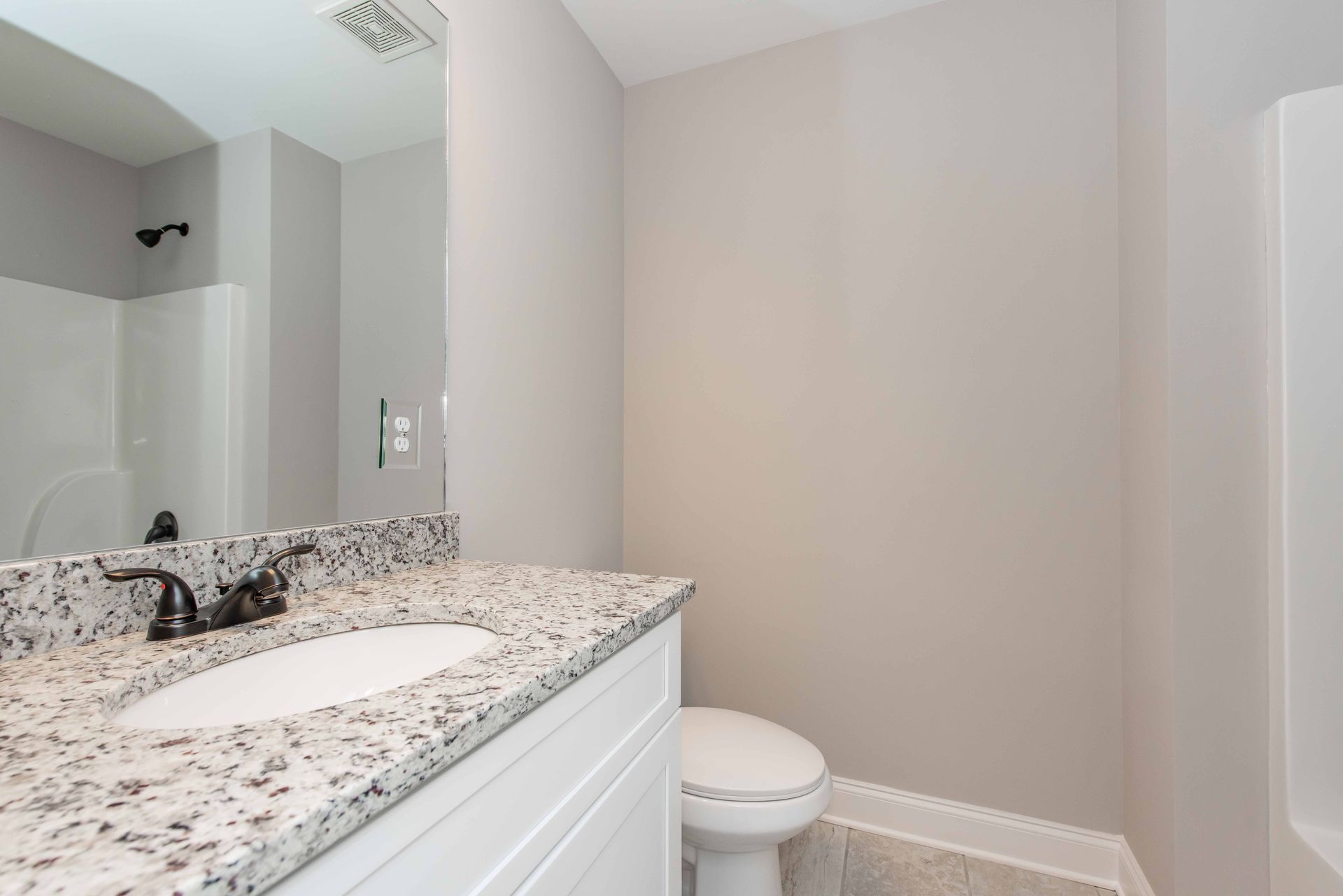 Modern bathroom with granite vanity, white sink, mirror, and toilet against beige walls