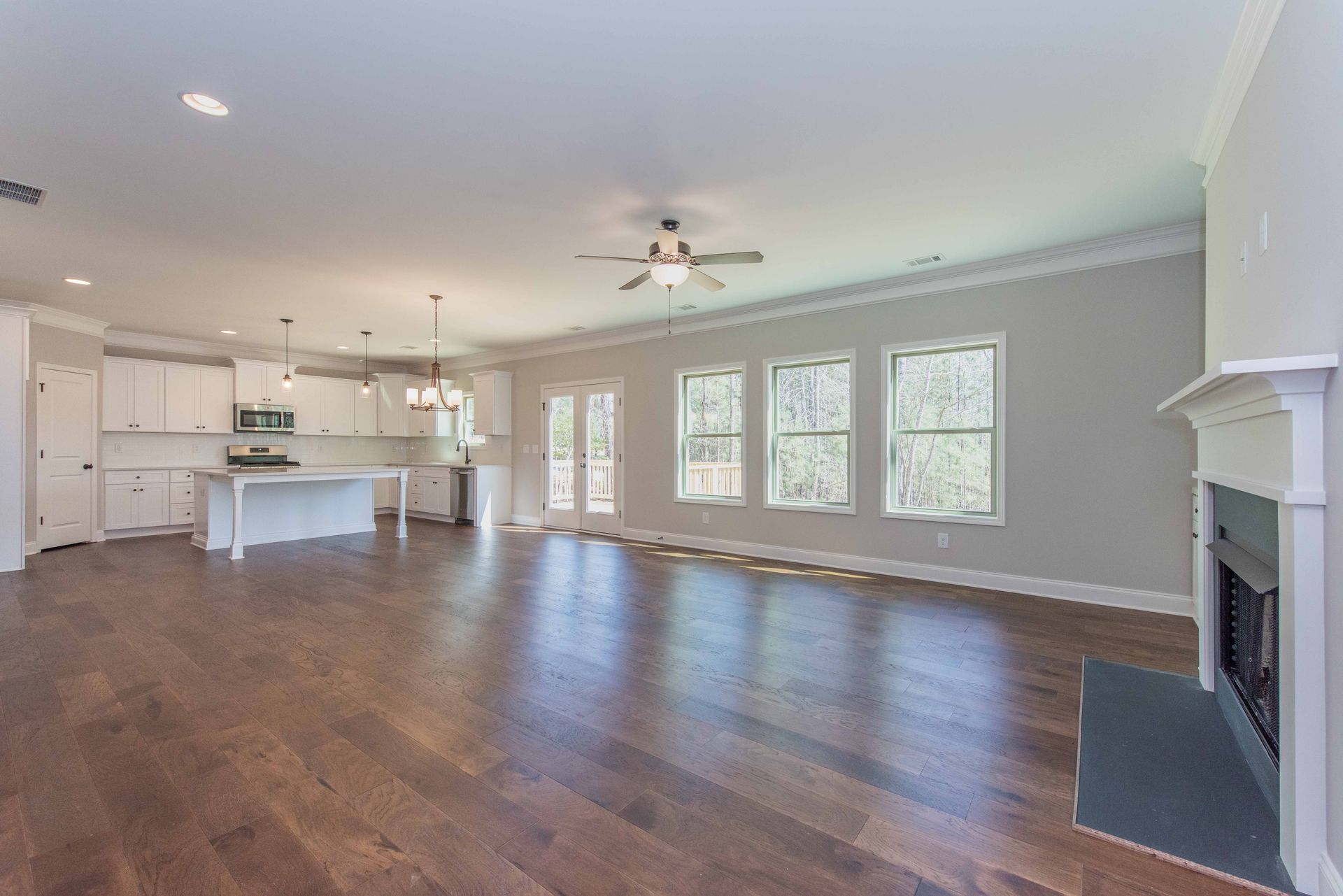 Spacious open-plan living room with hardwood floors, kitchen island, large windows, and fireplace