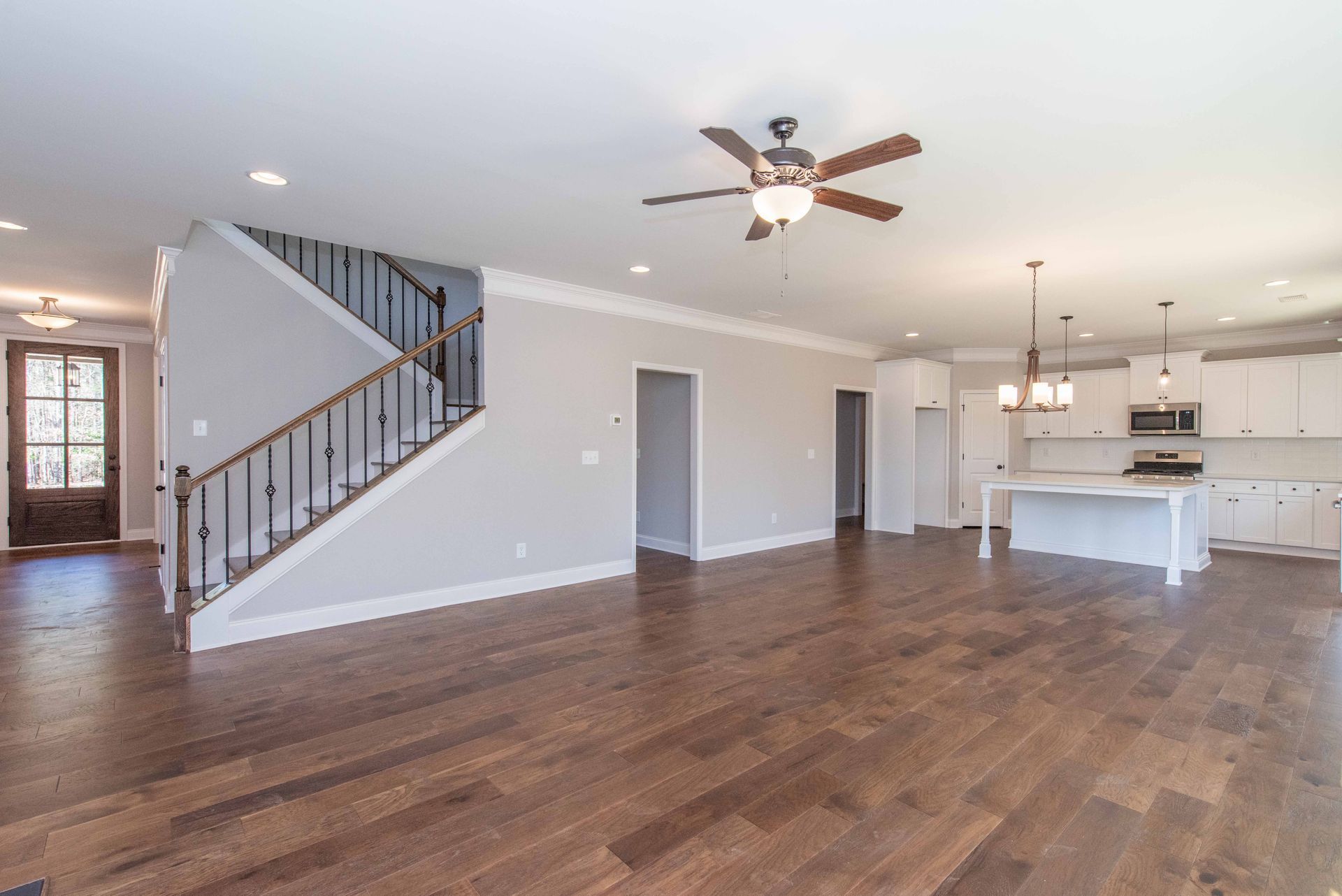 Open-concept living room with hardwood floors, staircase, ceiling fan, and kitchen island