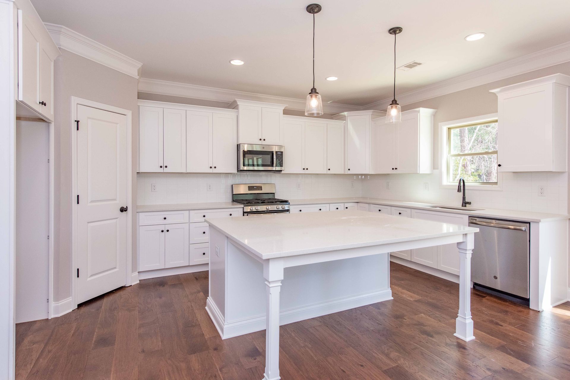 Bright white modern kitchen with large island, stainless appliances, pendant lights, and wood floors