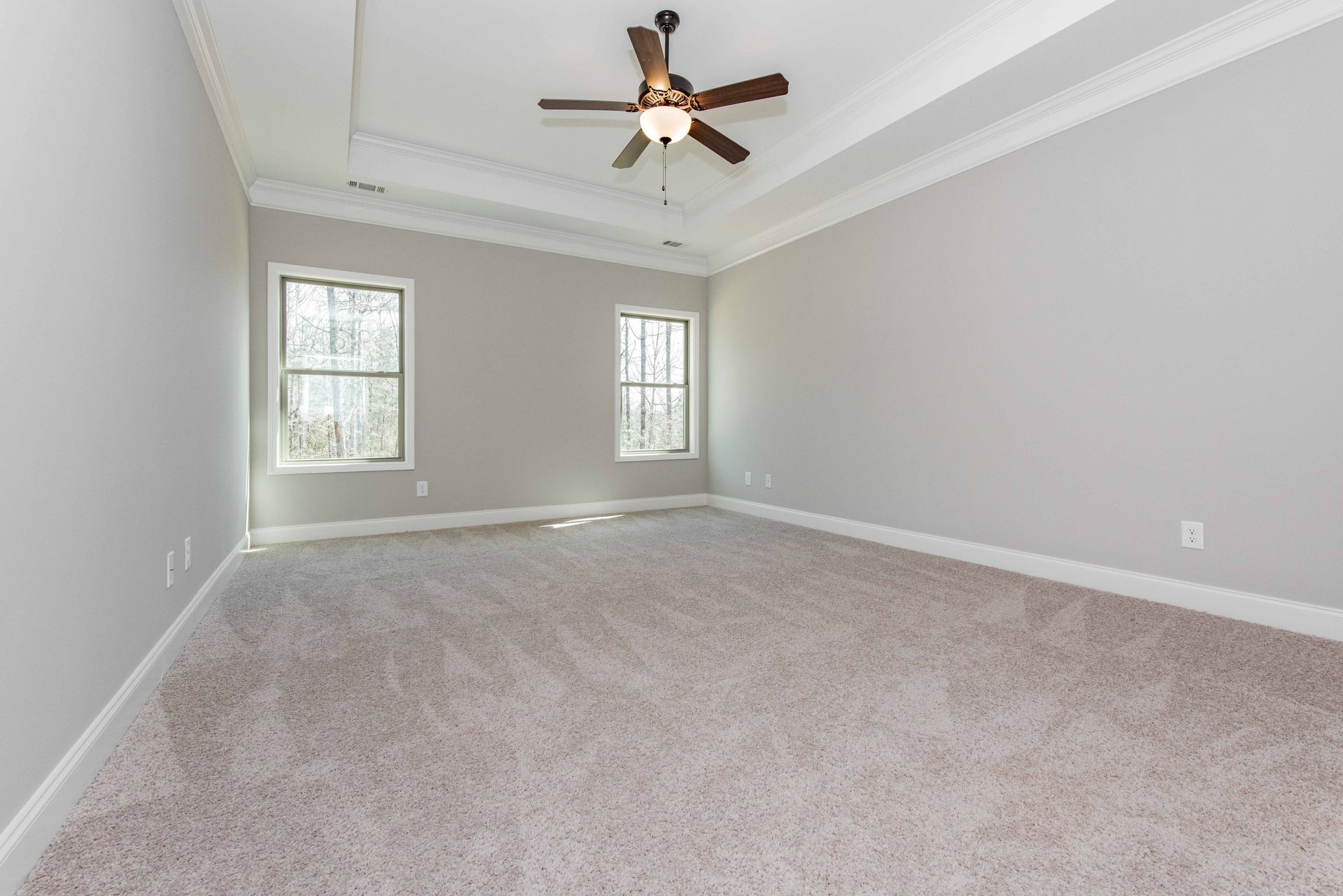 Empty gray bedroom with carpet, two windows, and a ceiling fan