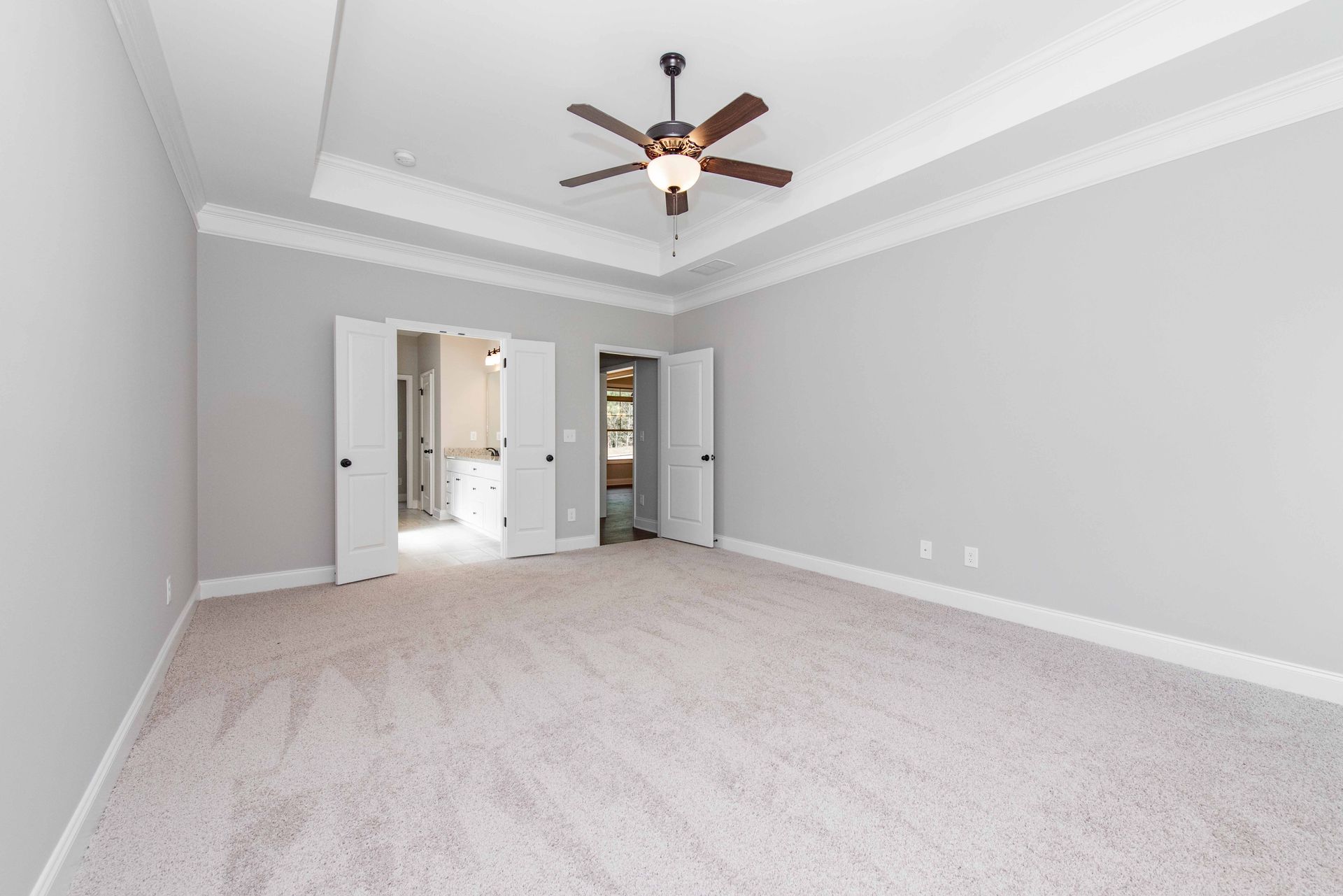 Empty gray bedroom with white trim, carpet, ceiling fan, and open doorway to a bathroom