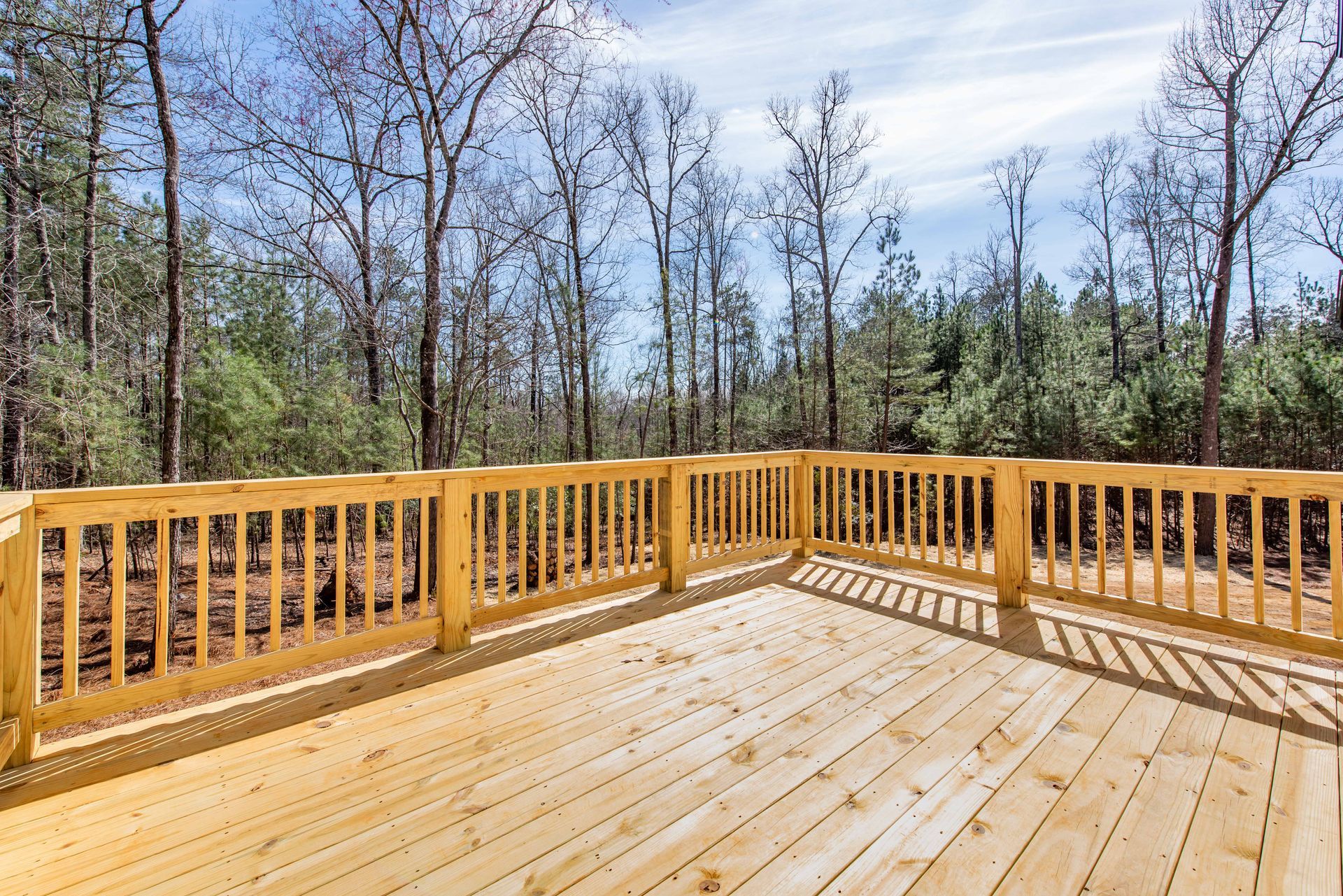 Wooden deck with railings overlooking a wooded backyard under a bright blue sky