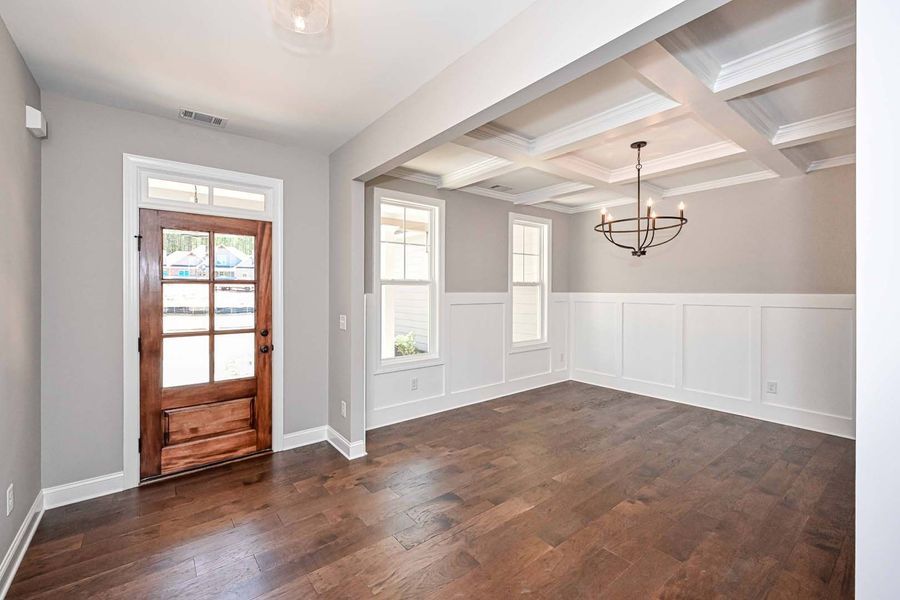 Empty dining room with dark wood floors, white wainscoting, and a coffered ceiling.