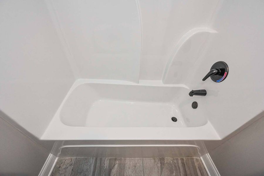 White bathtub in a shower enclosure with black faucet and drain.