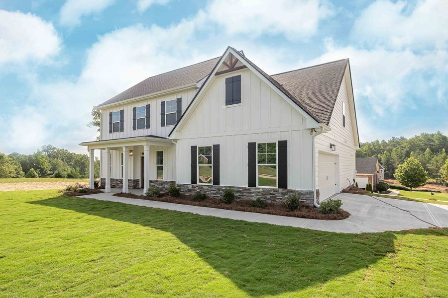 White farmhouse with black shutters, green lawn, and blue sky.