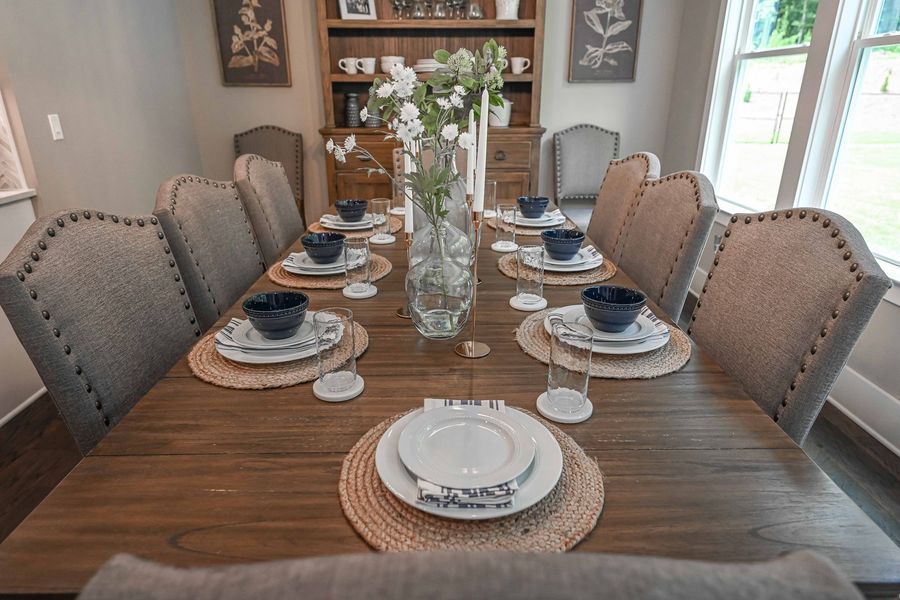 Dining room table set for a meal, with chairs, place settings, centerpiece, and a built-in hutch.