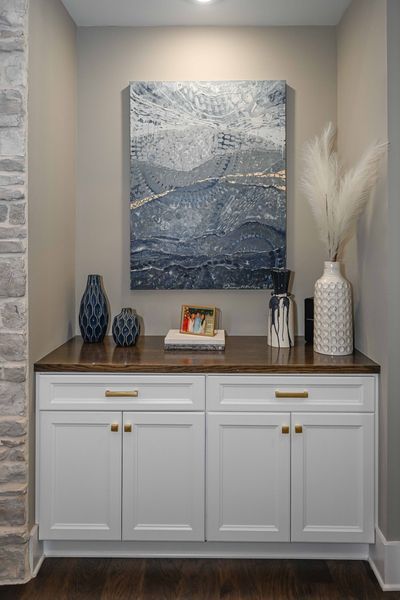 White cabinet with a dark countertop, decorated with vases and artwork.