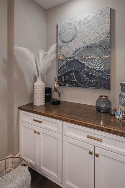 Built-in white cabinets with a dark wood countertop, decor, and artwork in a neutral-toned room.