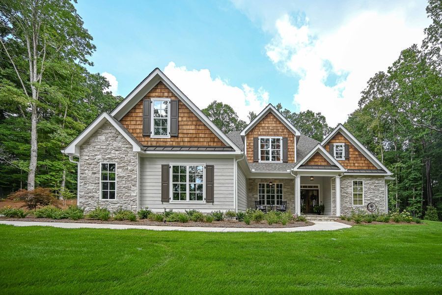 A single-story house with light-colored siding, stone accents, and a green lawn under a blue sky.