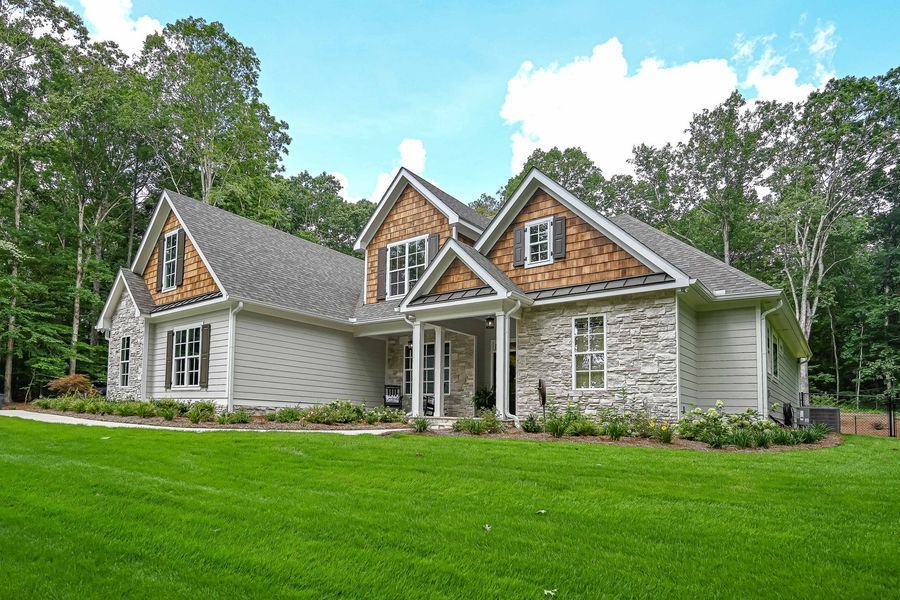 Gray house with stone accents, cedar shake roof, and green lawn.