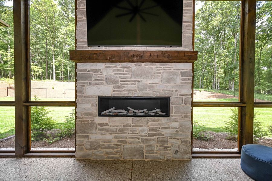 Fireplace with TV above, set against a forest backdrop, with stone surround and brown wooden beam.
