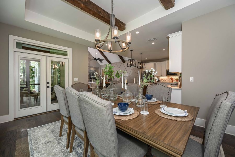Dining room with wooden table set for a meal, six upholstered chairs, open to a kitchen.