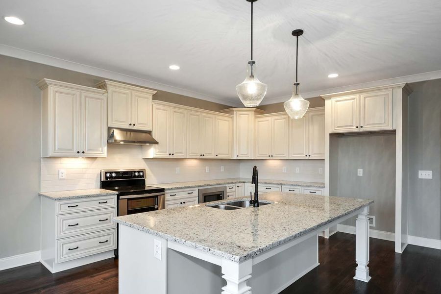 Cream-colored kitchen with granite island, dark cabinets, hardwood floors, and two hanging pendant lights.