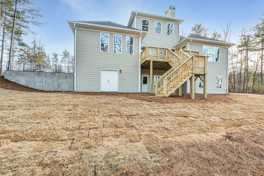 Beige house with wooden deck and stairs on a hillside. Overcast day.