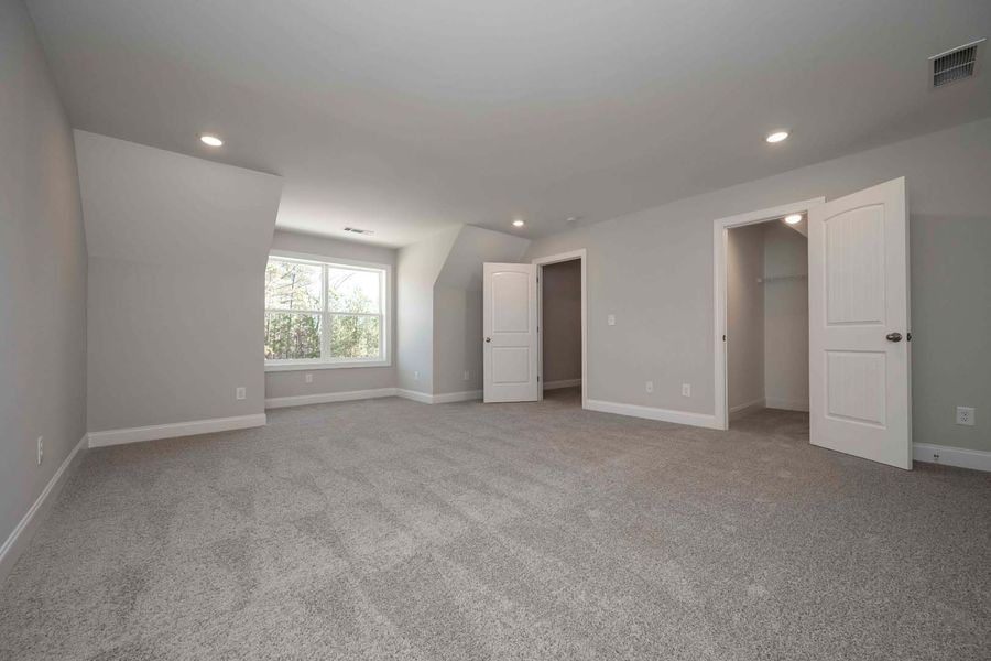 Empty bedroom with gray walls, carpet, and two white doors. Window with a view of trees.