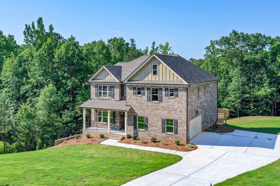 Two-story brick house with a long driveway, surrounded by trees on a sunny day.