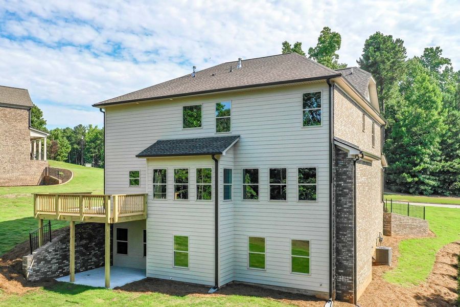 Back of a two-story home with a deck and brick accents, set against a green lawn and trees.
