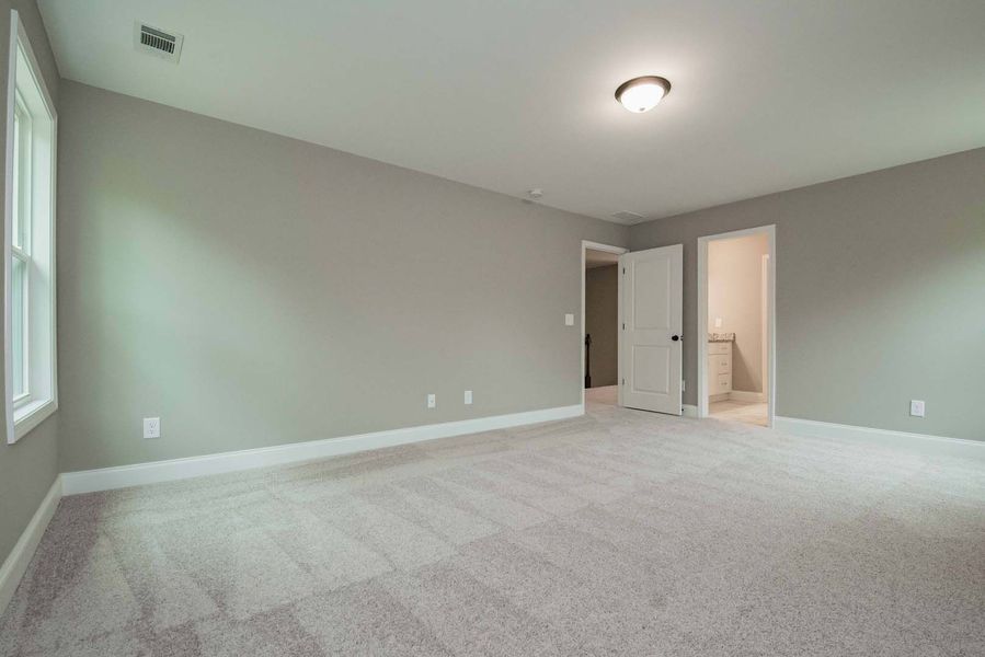 Empty bedroom with gray walls, white trim, and light carpet. A door opens to a bathroom.
