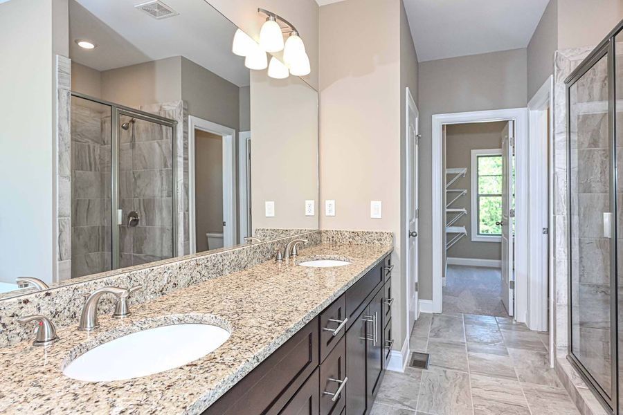 Bathroom with a long vanity, granite countertop, two sinks, large mirror, and walk-in shower.
