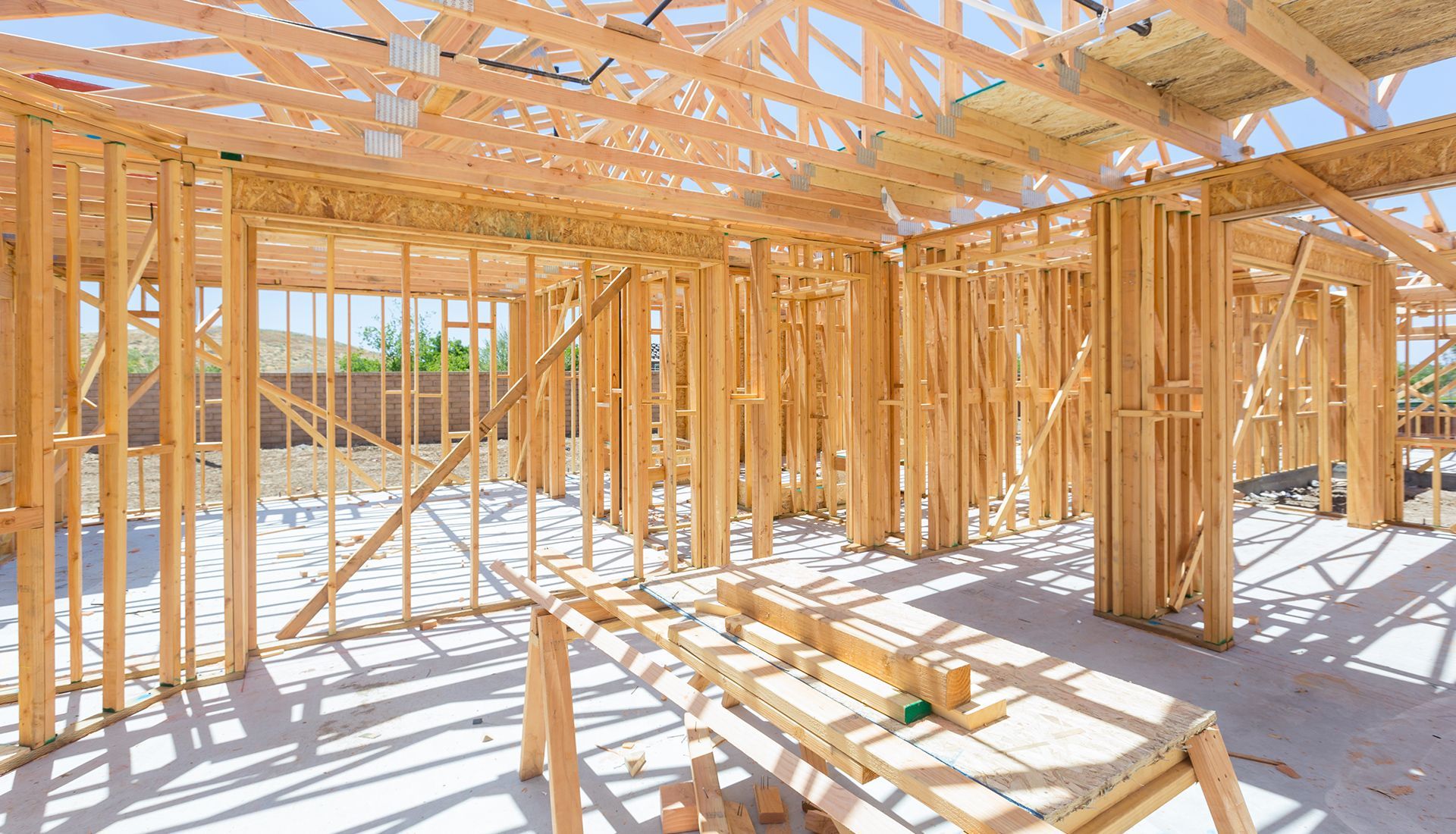 Wooden house frame construction site, interior view. Sunlight streams through the unfinished structure.