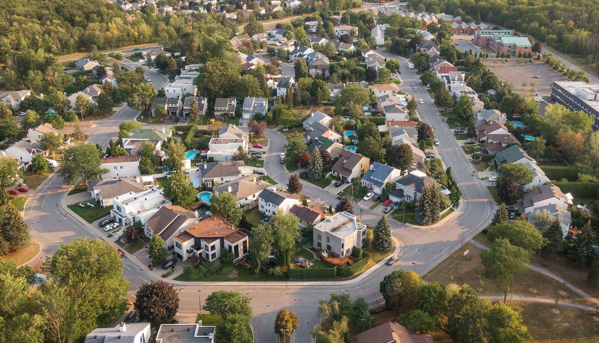Aerial view of a residential neighborhood with houses, roads, and trees under a sunny sky.