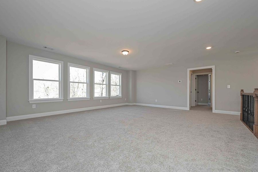 Empty, carpeted room with gray walls, several windows, and a doorway.