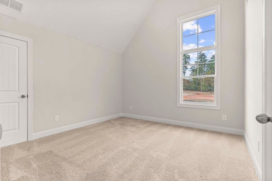 Empty bedroom with beige carpet, white walls, door, and window with blue sky view.