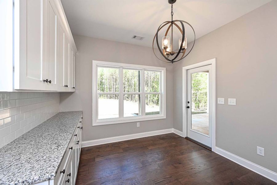 A bright kitchen with white cabinets, granite counters, and dark wood floors. Includes a window and door to outside.