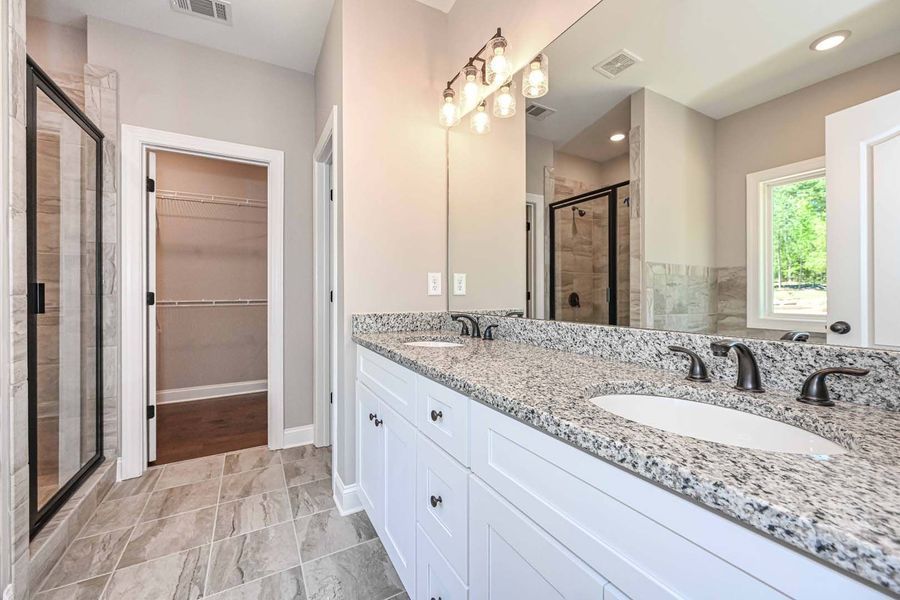 Bathroom with a white double vanity, granite countertop, large mirror, walk-in shower, and walk-in closet.