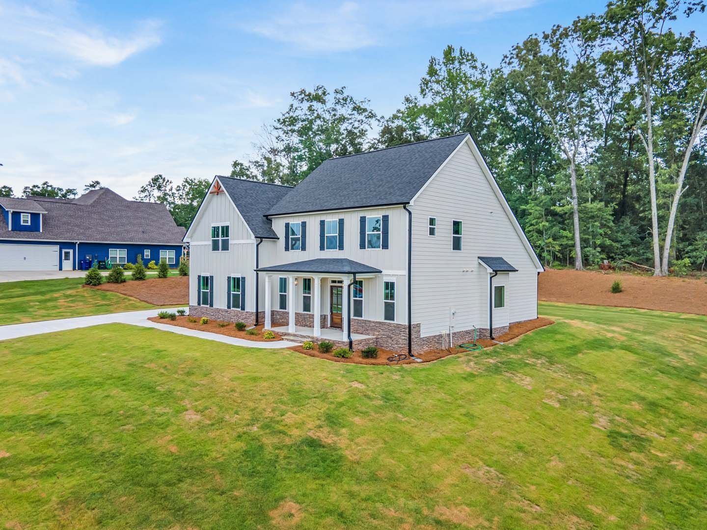 Two-story light gray house with black shutters, brick accents, and green lawn.