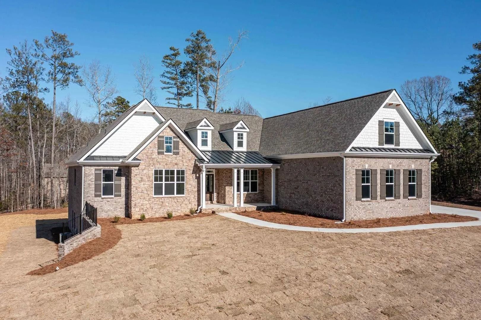 Brick house with three dormers and covered porch, brown and tan, on a sunny day.