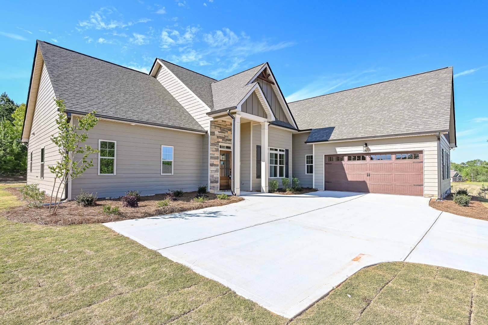 Beige house with brown roof, driveway, and garage door on a sunny day.