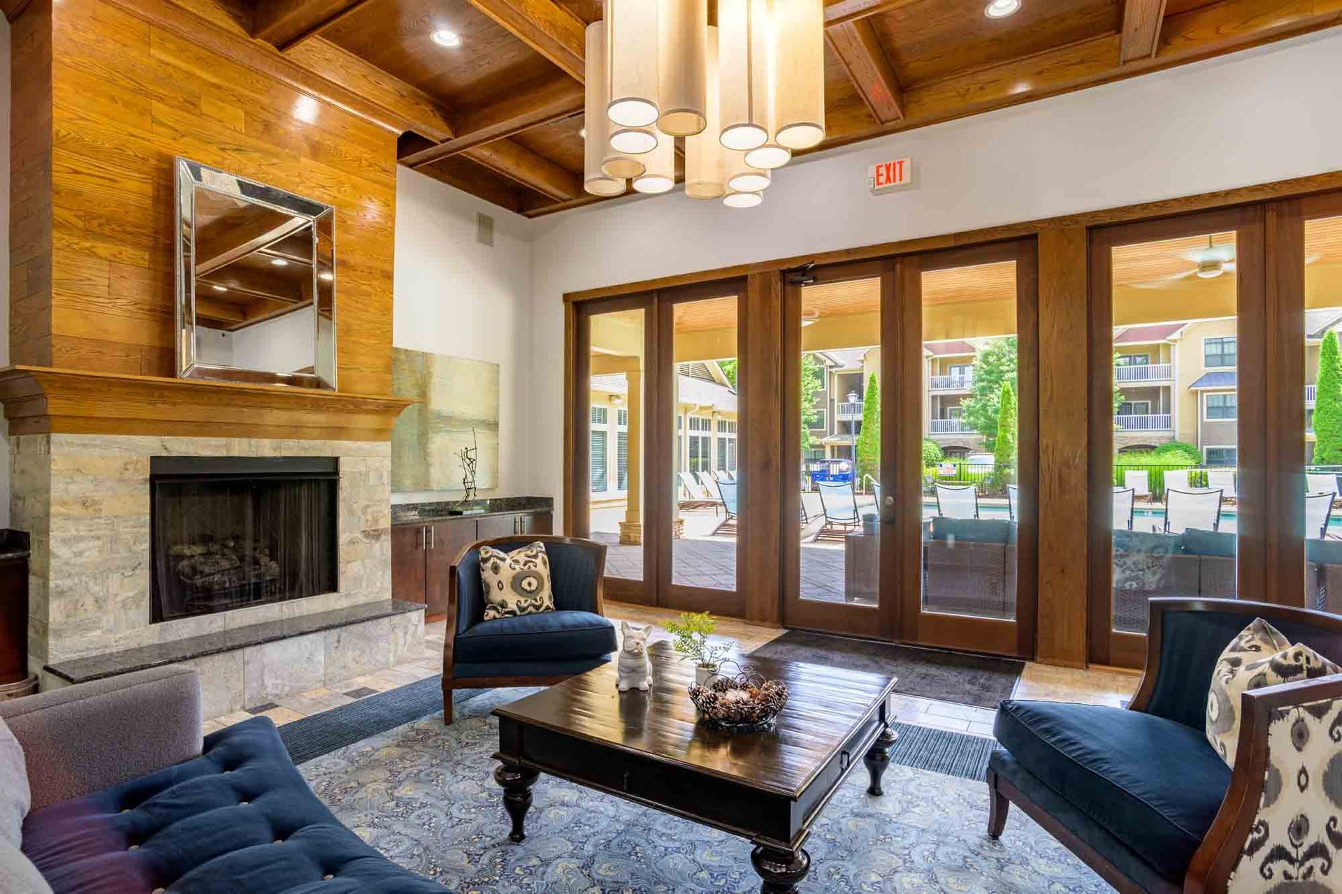 A luxurious lounge with fireplace, dark blue seating, and doors leading to an outdoor patio at Ansley Falls Apartment Homes in Charlotte, NC.