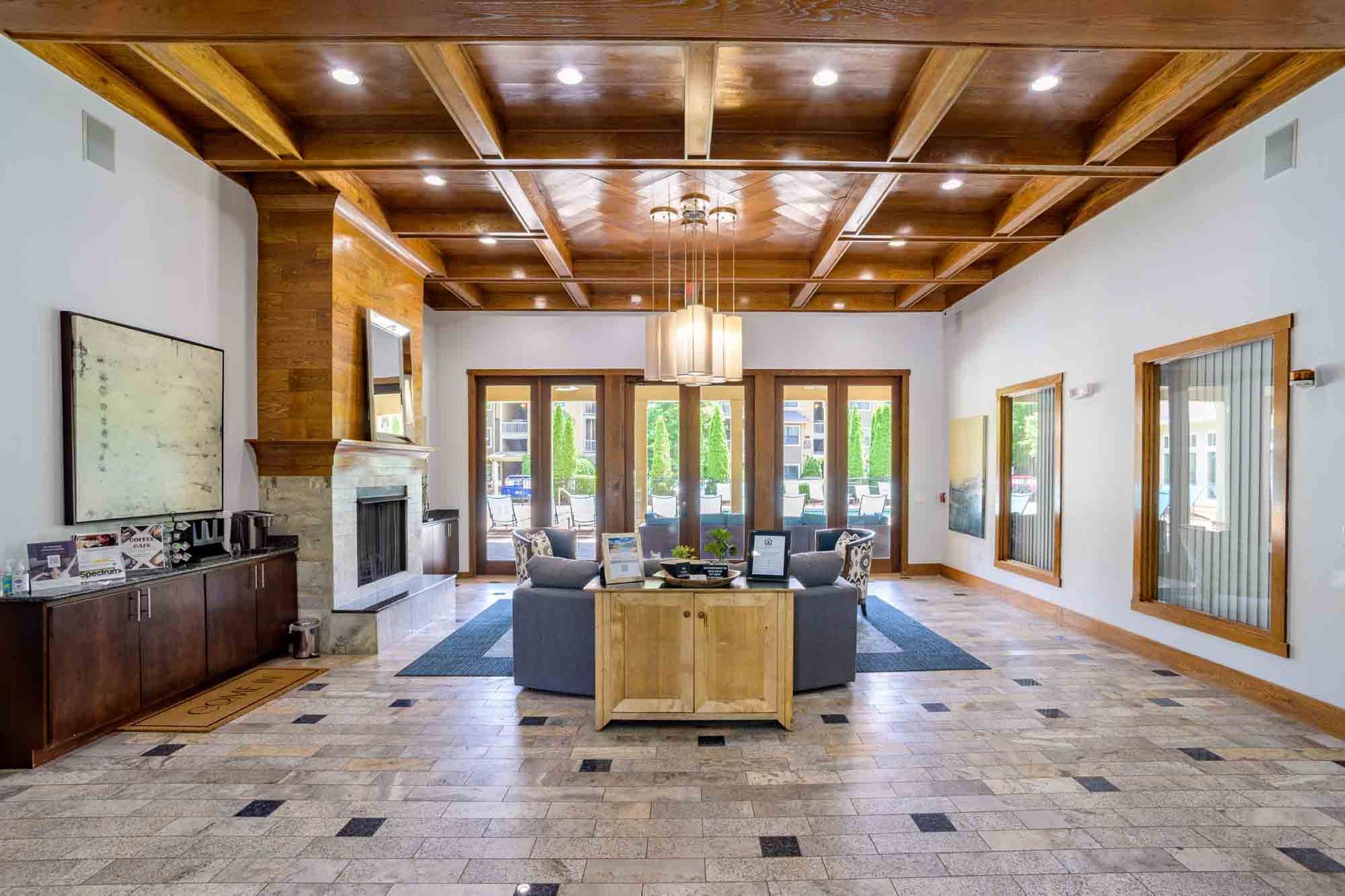 Lobby with stone floor, wood ceiling, fireplace, and doors leading to an outdoor patio at Ansley Falls Apartment Homes in Charlotte, NC.