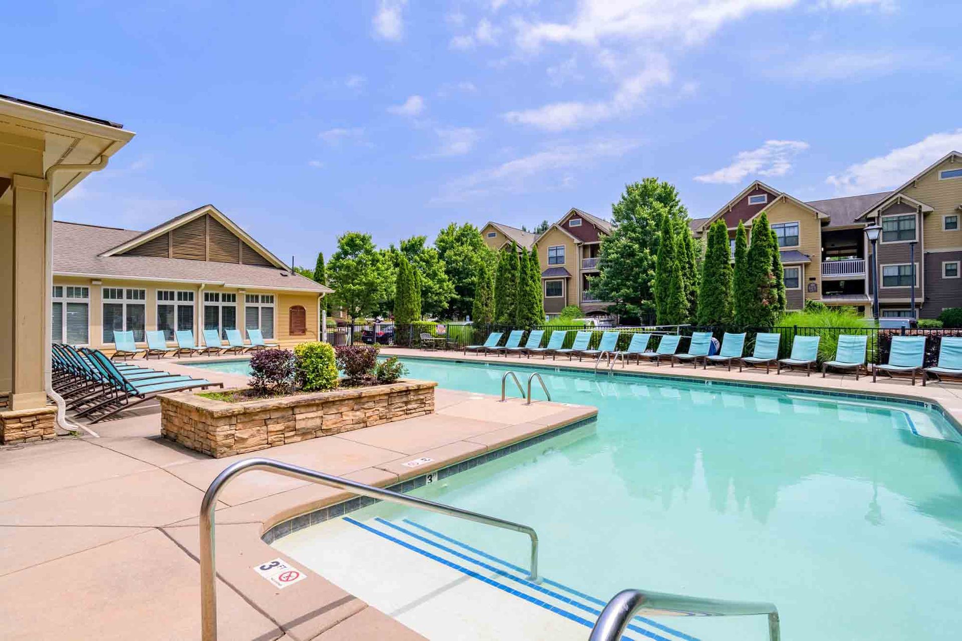 Swimming pool with lounge chairs, buildings in the background, blue sky at Ansley Falls Apartment Homes in Charlotte, NC.