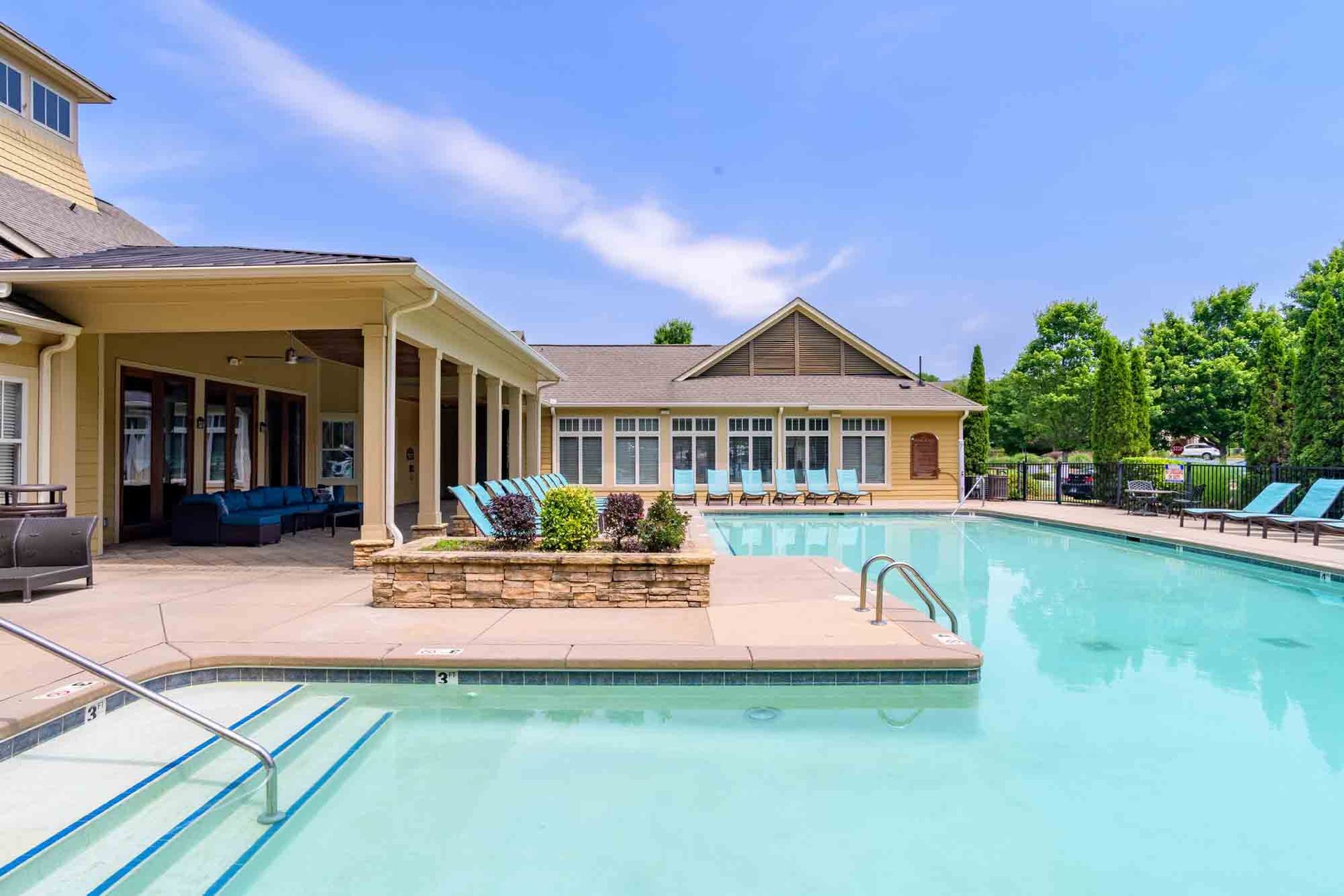 Pool area with turquoise water, beige buildings, and blue lounge chairs on a sunny day at Ansley Falls Apartment Homes in Charlotte, NC.