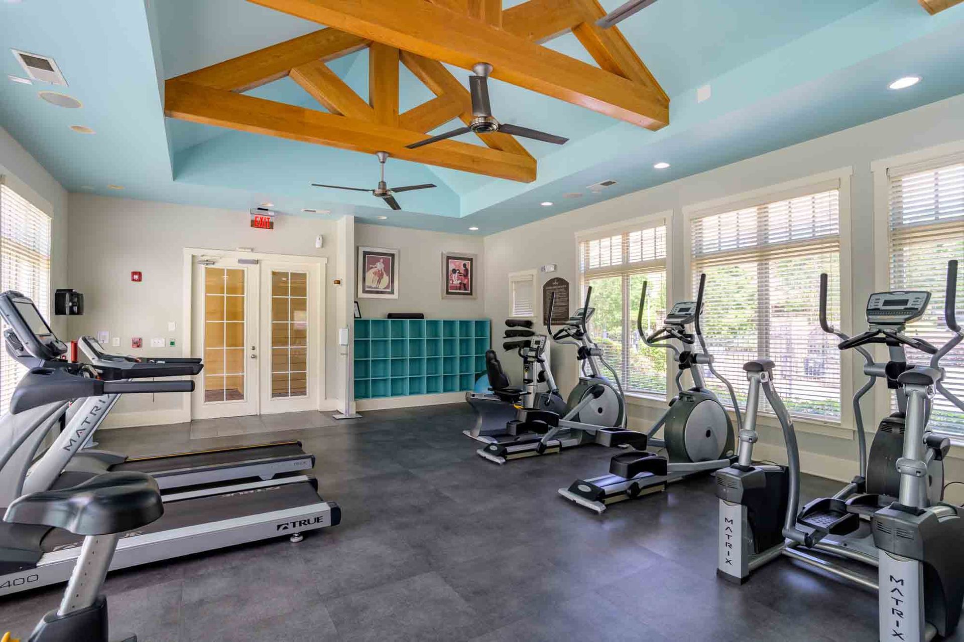 Gym with exercise equipment: treadmills, ellipticals, recumbent bikes. Blue ceiling with wooden beams at Ansley Falls Apartment Homes in Charlotte, NC.