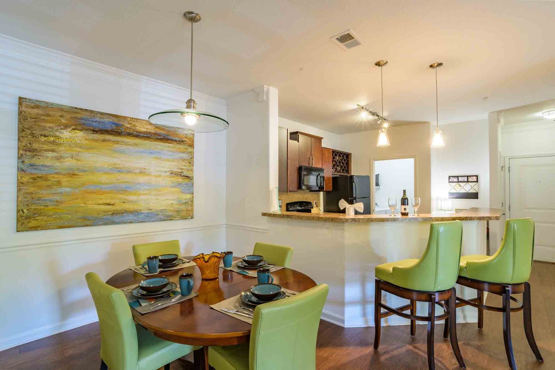 Dining room with round table, green chairs, and abstract art; kitchen with bar stools at Ansley Falls Apartment Homes in Charlotte, NC.