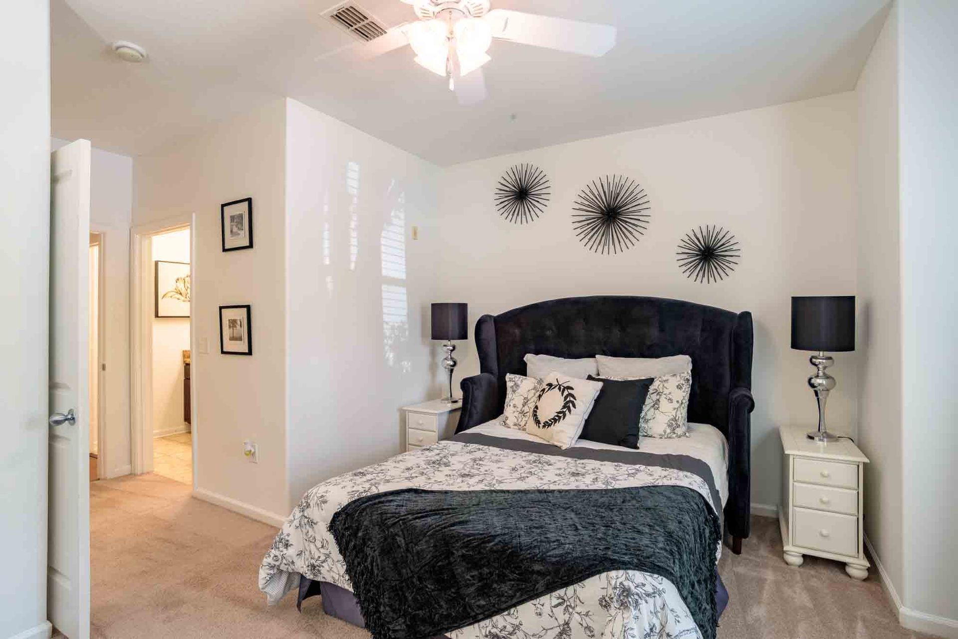 Bedroom with a black bed, white nightstands, and starburst wall decor; neutral colors at Ansley Falls Apartment Homes in Charlotte, NC.