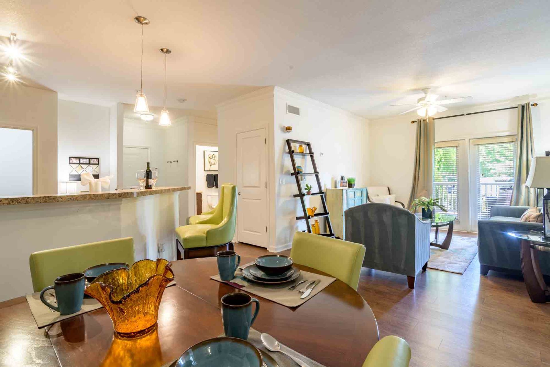 Dining area with round table, adjacent to a living room. Green and blue accents, neutral walls at Ansley Falls Apartment Homes in Charlotte, NC.