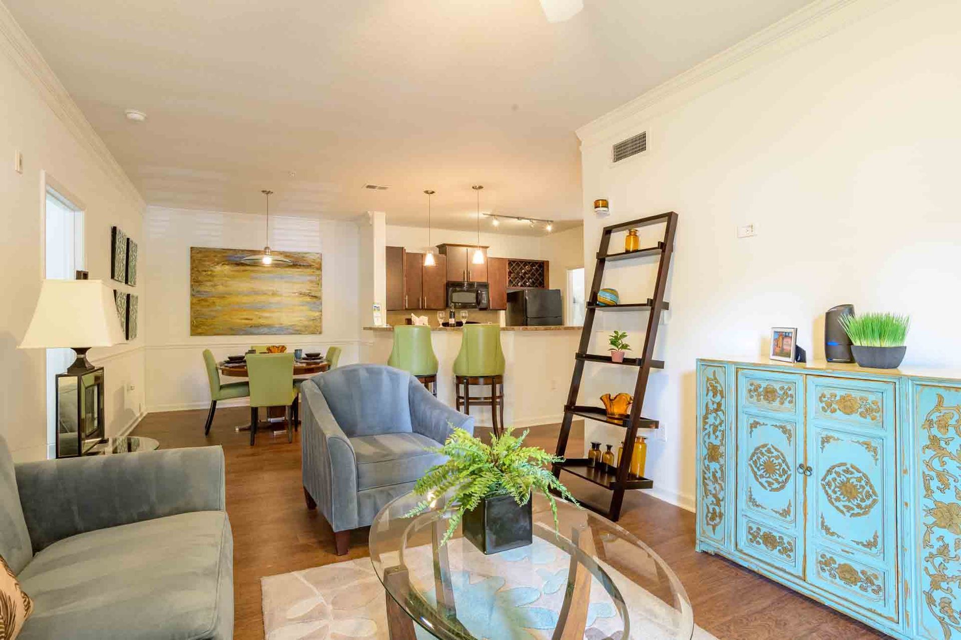 Living room with blue sofa and chair, wooden shelves, dining area, and kitchen at Ansley Falls Apartment Homes in Charlotte, NC.