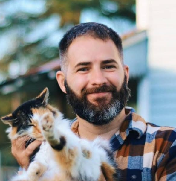 A man with a beard is holding a cat in his arms