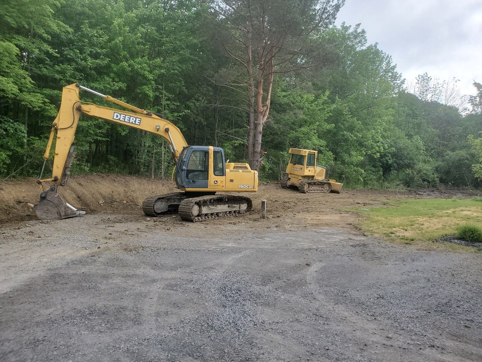 Yellow excavator and bulldozer on a dirt road beside dense green trees