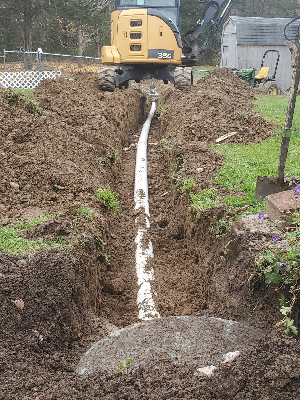 Backhoe on a dirt trench with a white pipe laid along the center in a yard.